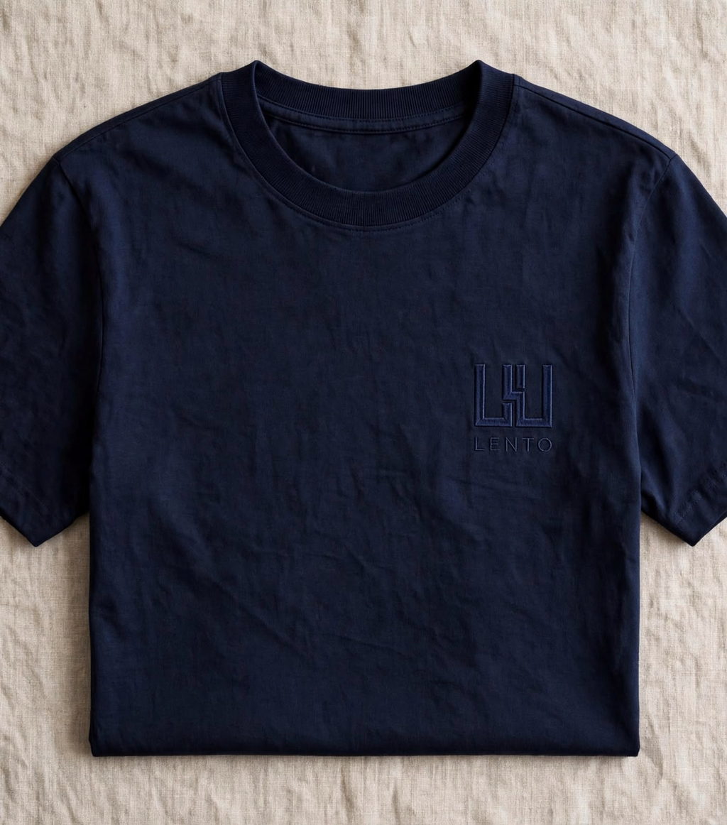 A navy heavyweight cotton t-shirt laid flat on natural linen, with a tonal embroidered mark on the chest.